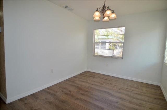 spare room featuring an inviting chandelier and dark hardwood / wood-style flooring