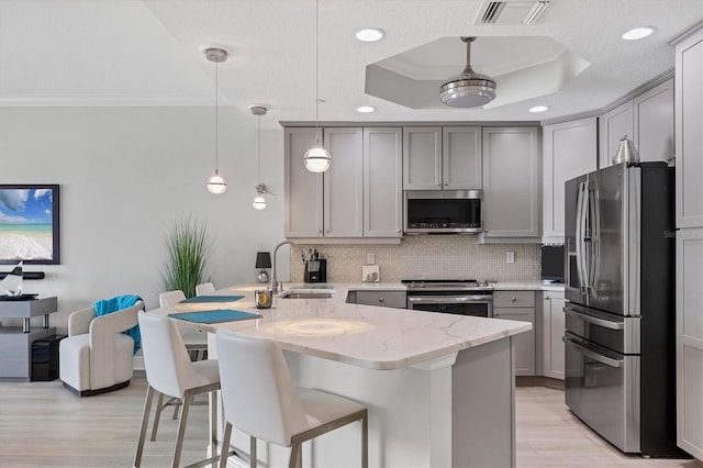 kitchen with pendant lighting, stainless steel appliances, gray cabinetry, and light stone countertops