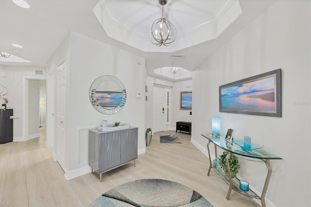 hall featuring a tray ceiling, light wood-type flooring, crown molding, and a notable chandelier