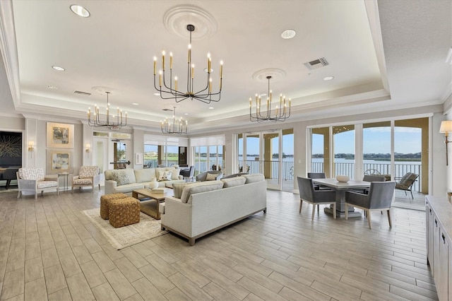 living room with a water view, a chandelier, light hardwood / wood-style floors, and a raised ceiling