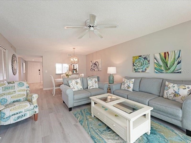 living room with a textured ceiling, light wood finished floors, and ceiling fan with notable chandelier