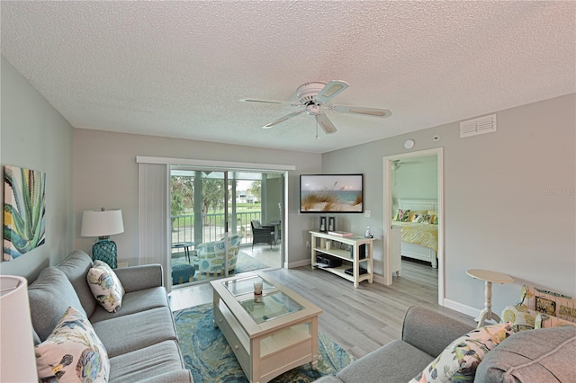 living room with visible vents, baseboards, light wood-style flooring, ceiling fan, and a textured ceiling