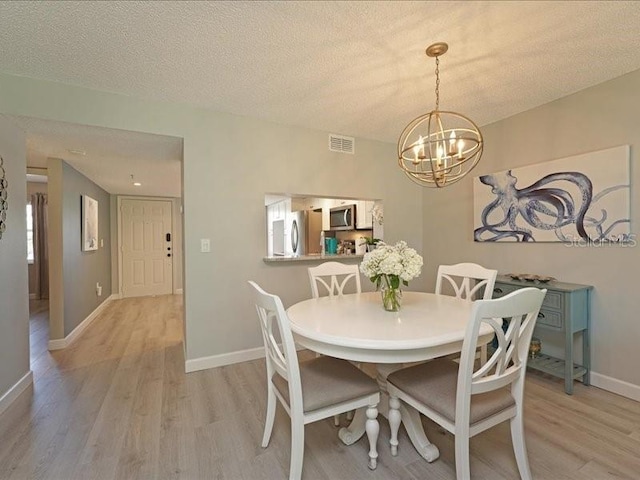 dining room with light wood-type flooring, visible vents, a textured ceiling, and baseboards