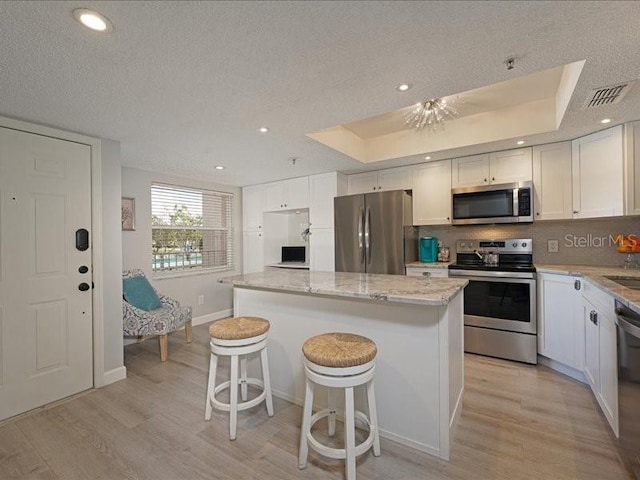 kitchen with a raised ceiling, appliances with stainless steel finishes, a kitchen island, and white cabinetry