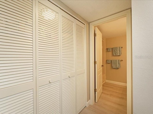 hallway featuring light wood-style floors, a textured ceiling, and baseboards