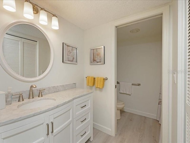 bathroom with baseboards, toilet, wood finished floors, a textured ceiling, and vanity