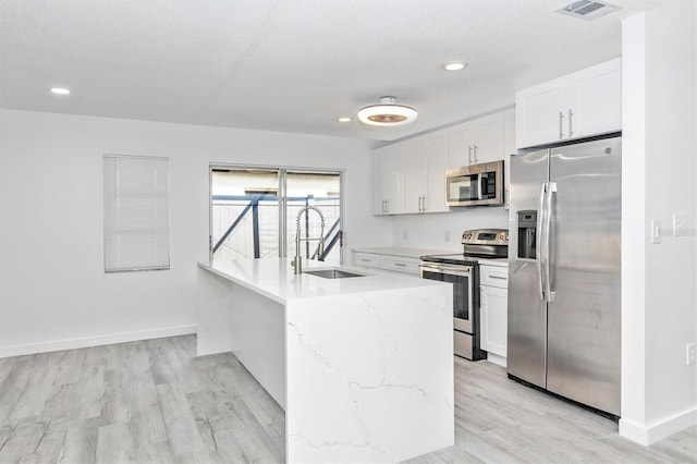 kitchen featuring light stone countertops, light wood finished floors, a sink, stainless steel appliances, and white cabinets