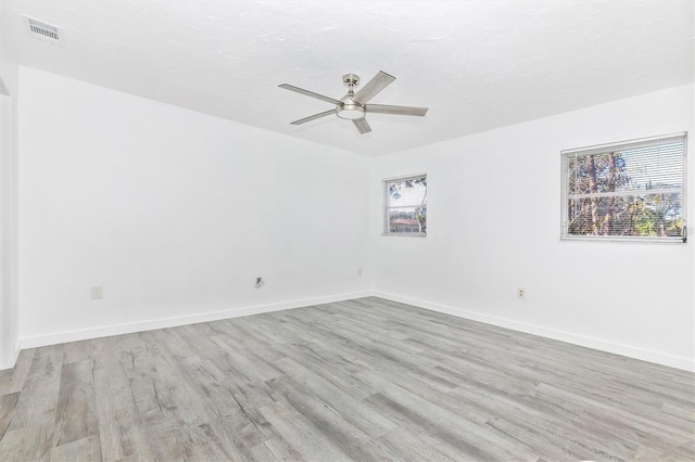 spare room with ceiling fan, visible vents, baseboards, and wood finished floors