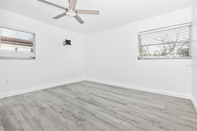 empty room with a wealth of natural light, baseboards, wood finished floors, and a ceiling fan