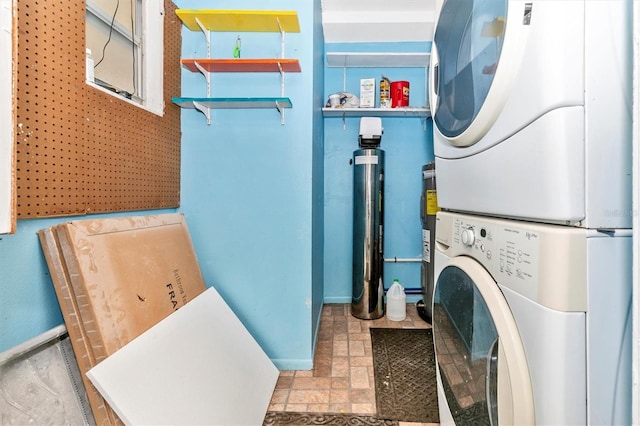 washroom featuring stacked washer / drying machine, baseboards, and laundry area