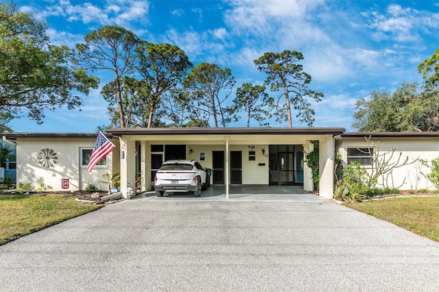 ranch-style house with aphalt driveway, an attached carport, a front yard, and stucco siding