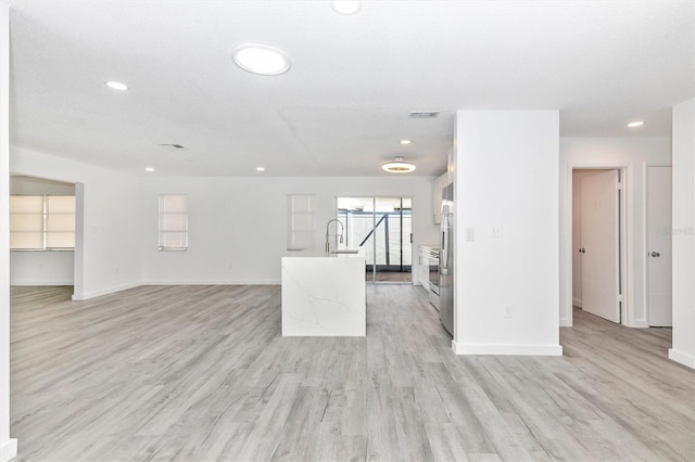 unfurnished living room with a sink, visible vents, baseboards, and light wood-style floors