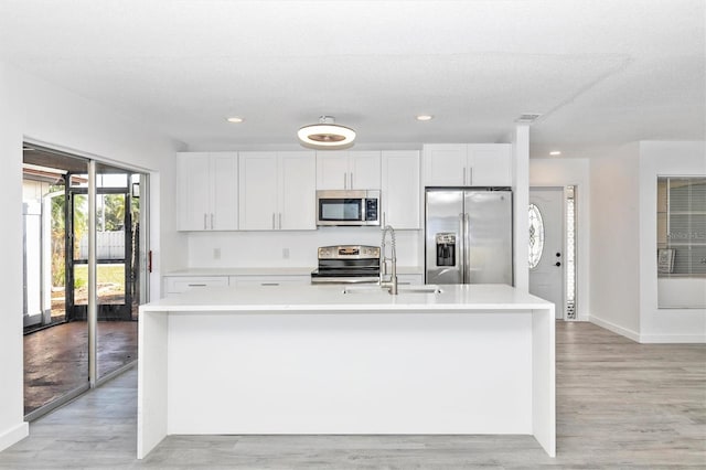 kitchen featuring light wood-style flooring, an island with sink, a sink, stainless steel appliances, and white cabinets