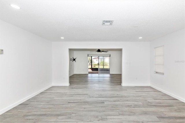 spare room with baseboards, light wood finished floors, and a textured ceiling