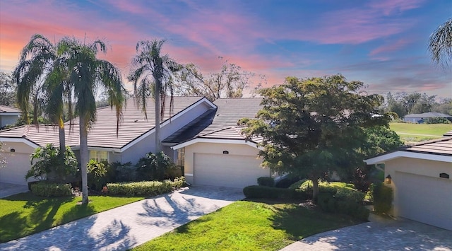 single story home with a garage, a tile roof, a yard, driveway, and stucco siding