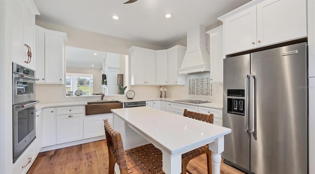 kitchen featuring custom exhaust hood, stainless steel appliances, light countertops, white cabinetry, and a sink