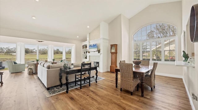 dining area featuring high vaulted ceiling, a wealth of natural light, a fireplace, and light wood-style flooring