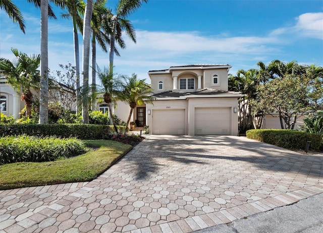 mediterranean / spanish home featuring an attached garage, a tiled roof, decorative driveway, and stucco siding