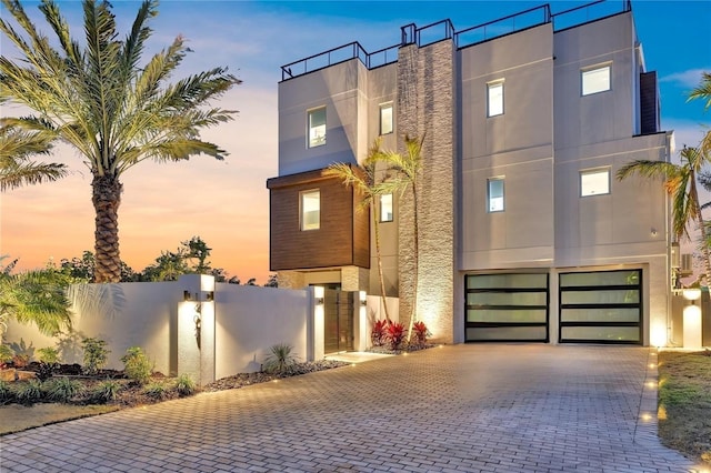 contemporary house with a garage, decorative driveway, fence, and stucco siding