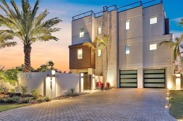 contemporary house featuring stucco siding, decorative driveway, a garage, and fence