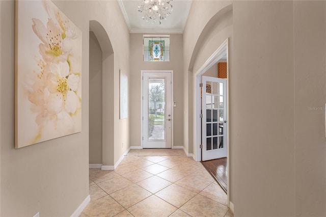 entryway with light tile patterned floors, baseboards, arched walkways, and crown molding