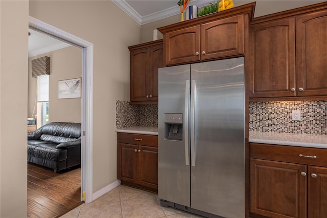 kitchen with stainless steel refrigerator with ice dispenser, light tile patterned floors, light countertops, decorative backsplash, and ornamental molding