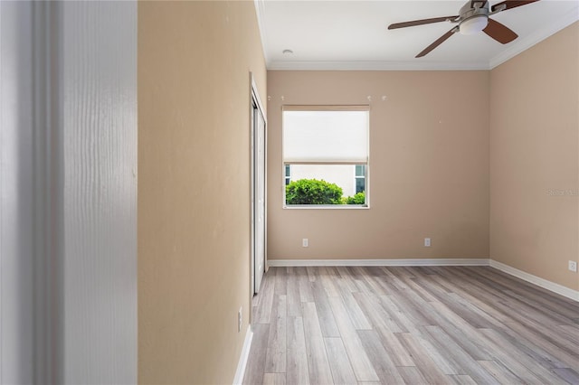 spare room featuring light wood finished floors, ornamental molding, a ceiling fan, and baseboards