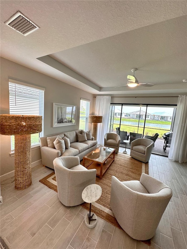 living room featuring ceiling fan, a tray ceiling, and a textured ceiling