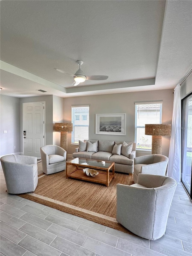 living room featuring a textured ceiling, a raised ceiling, and ceiling fan