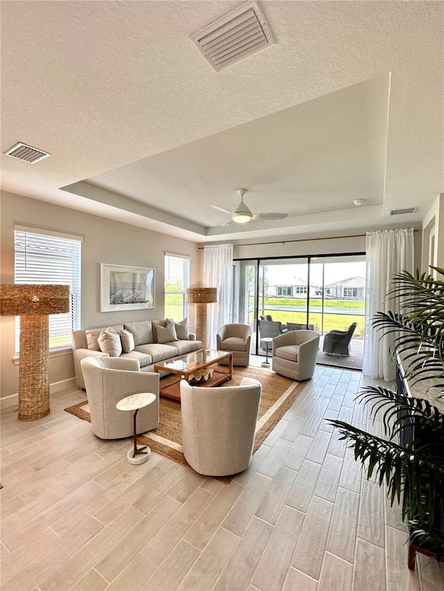 living room featuring a tray ceiling, a textured ceiling, and ceiling fan