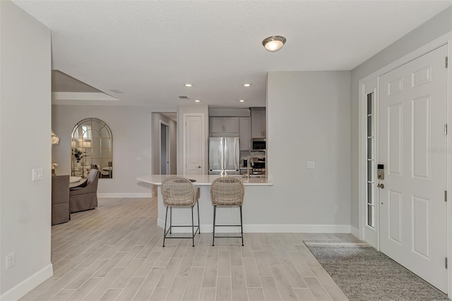 kitchen with stainless steel appliances, gray cabinets, a kitchen breakfast bar, and light hardwood / wood-style floors