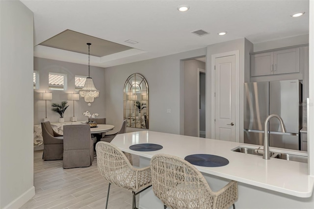 kitchen featuring gray cabinets, pendant lighting, stainless steel refrigerator, sink, and light wood-type flooring