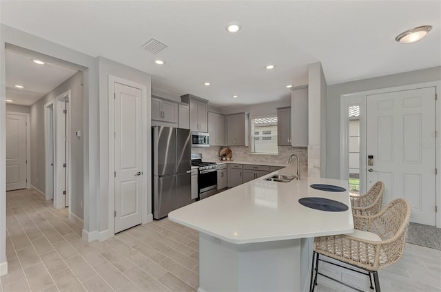 kitchen featuring sink, a breakfast bar area, appliances with stainless steel finishes, gray cabinetry, and kitchen peninsula