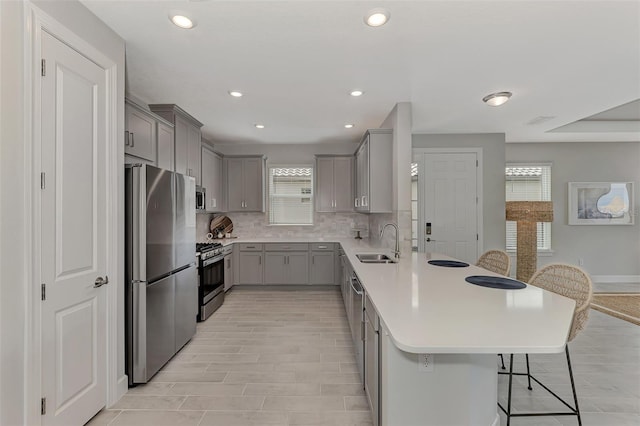 kitchen with sink, a breakfast bar, gray cabinetry, stainless steel appliances, and decorative backsplash