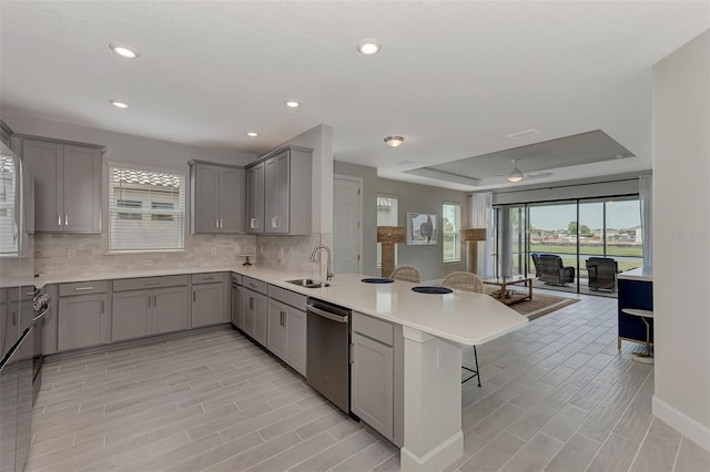 kitchen with gray cabinets, dishwasher, sink, a kitchen bar, and kitchen peninsula