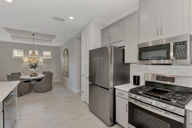 kitchen with gray cabinetry, tasteful backsplash, a raised ceiling, pendant lighting, and stainless steel appliances