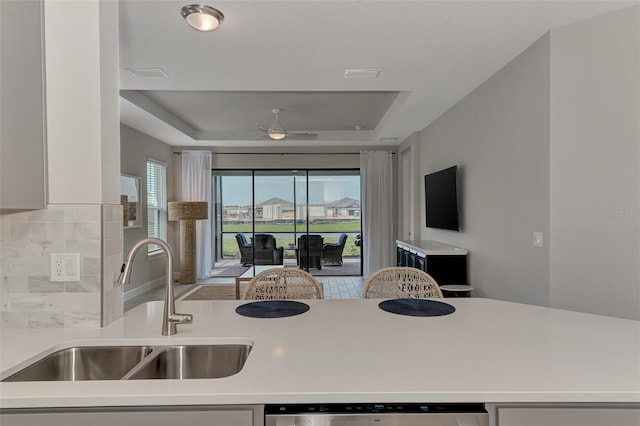 kitchen featuring ceiling fan, a tray ceiling, dishwasher, and sink