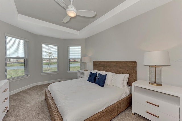 bedroom with a tray ceiling, light colored carpet, and ceiling fan