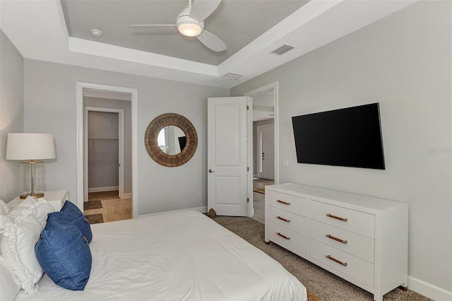 carpeted bedroom with ceiling fan, a walk in closet, and a tray ceiling