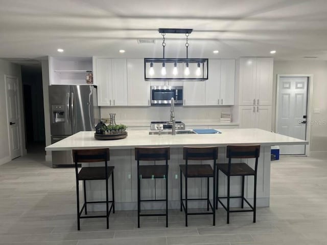 kitchen featuring appliances with stainless steel finishes, a kitchen bar, white cabinets, and a center island with sink