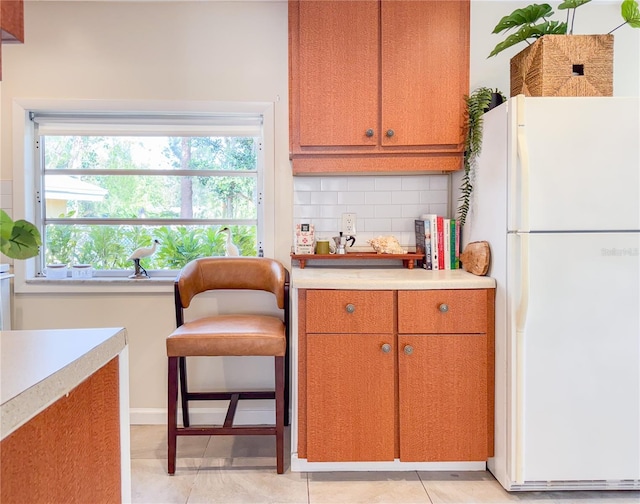 kitchen featuring white refrigerator, light tile patterned flooring, and decorative backsplash