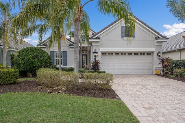 view of front of home with decorative driveway, an attached garage, and stucco siding