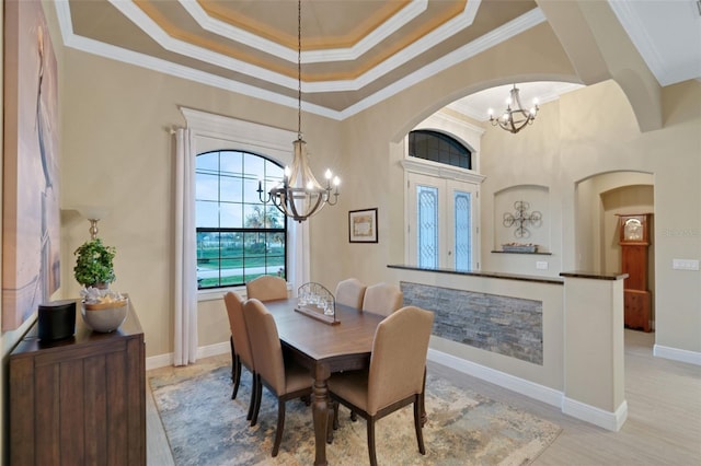 dining space with ornamental molding, a tray ceiling, a notable chandelier, and light wood finished floors