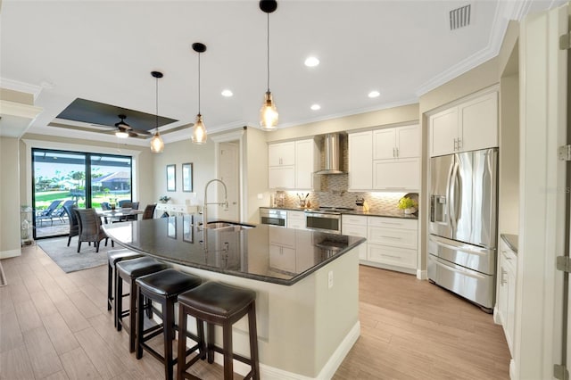 kitchen with stainless steel appliances, white cabinetry, a sink, an island with sink, and wall chimney exhaust hood