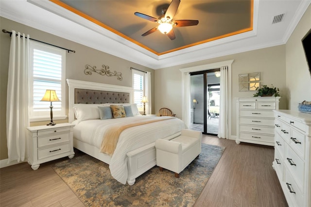 bedroom featuring ceiling fan, visible vents, access to outside, a tray ceiling, and dark wood finished floors