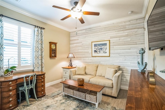 living room with baseboards, ceiling fan, an accent wall, wood finished floors, and crown molding