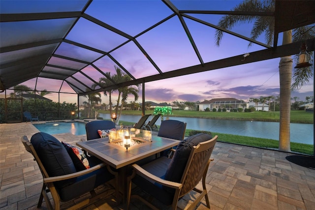 patio terrace at dusk featuring a water view, a lanai, and an outdoor pool