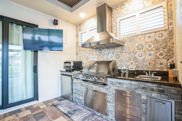 kitchen featuring range hood, backsplash, stone finish flooring, a sink, and dark stone countertops