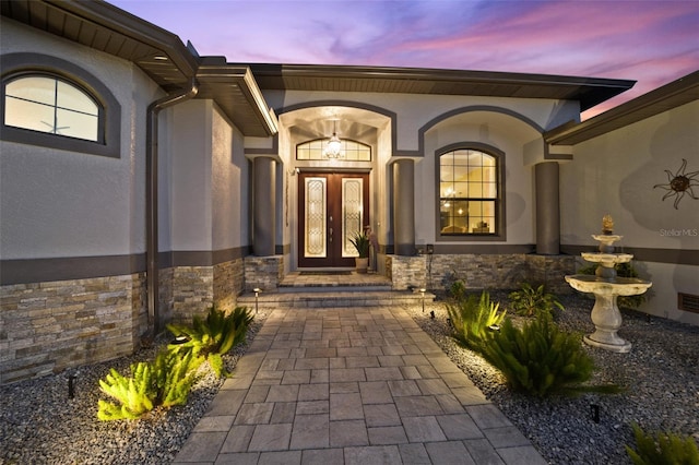 property entrance featuring stucco siding, stone siding, and french doors