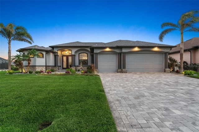 prairie-style house with a garage, decorative driveway, a yard, and stucco siding